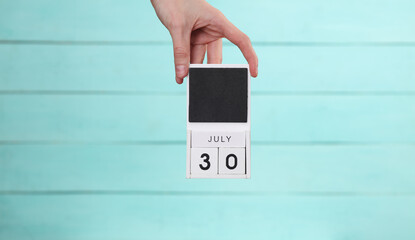 Woman's hand holds wooden calendar with date july 30 on blue wooden background