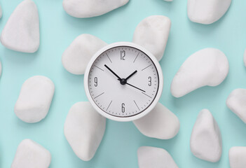 Fototapeta na wymiar Clock on a blue background with pebbles.