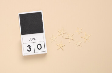 White wooden calendar with the date june 29 and sea stars on a beige background. Summer time. Top view
