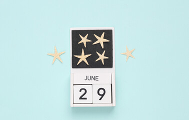 White wooden calendar with the date june 29 and sea stars on a blue background. Summer time. Top view