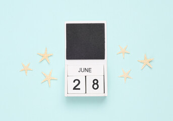 White wooden calendar with the date june 28 and sea stars on a blue background. Summer time. Top view
