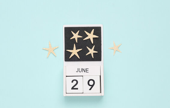 White wooden calendar with the date june 29 and sea stars on a blue background. Summer time. Top view