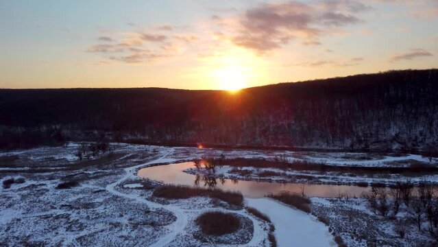 Aerial speed-up footage of sunset sun shine in winter landscape with river curve and scenic reflection. Snowing on Siverskyi Donets river valley in Ukraine