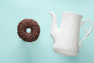 Ceramic teapot with chocolate donut on blue background