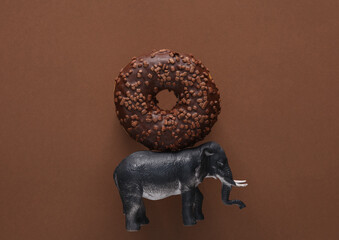 Toy elephant with chocolate donut on brown background