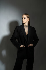 Fashion portrait of a young girl in a black suit, black bra and transparent top. The model poses on a white background. Art makeup. Photography in the studio.