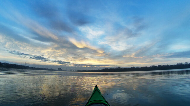 View from bow (prow) of green kayak at dramatic buatiful sunset over Danube river at cold season. Winter kayaking