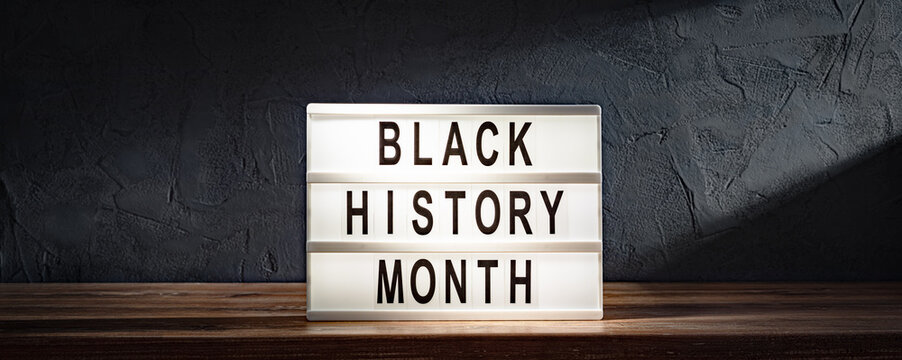 Black History Month words on lightbox on wooden shelf on black stone wall background
