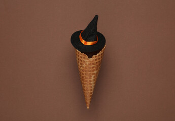 Halloween concept. Waffle cone with witch hat on brown background