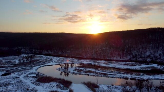 Aerial left to right sunset sun shine above wintry river curve with scenic reflection. Zmiyevsky region on Siverskyi Donets river valley in Ukraine