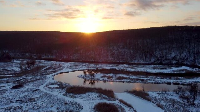 Aerial arc view on sunset sun shine above wintry landscape on  river curve with scenic reflection. Zmiyevsky region on Siverskyi Donets river valley in Ukraine