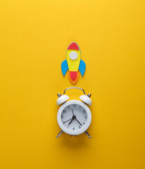 Alarm clock with a rocket on a yellow background. Startup, education concept