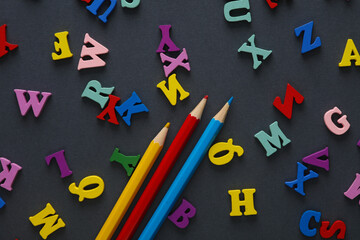 Colored pencils and many letters on a gray background. Education concept