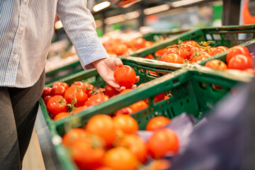 Woman hand picking up tomatoes in a supermarket. Healthy diet concept. Grocery shopping.