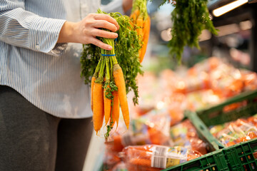 Woman hand holding carrots in a supermarket. Healthy diet concept. Grocery shopping.