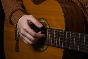 Fototapeta premium Female hands play an acoustic guitar on a black background. To play guitar