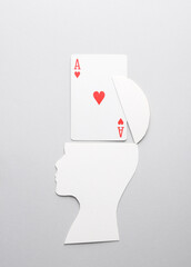 Paper-cut silhouette of head with ace of hearts on gray background. Gambling addiction