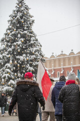 Mężczyzna niosący flagę Polski na tle bożonarodzeniowej choinki. Flaga Polski na tle choinki. 