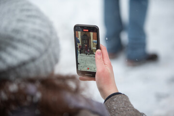Kobieta robiąca zdjęcie w śnieżny dzień. Kobieta nagrywająca telefonem zimowe spotkanie. Mobilne nagrywanie - obrazy, fototapety, plakaty