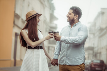 International couple in love drinking coffee walking around the city, holding hand