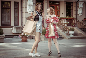 Two laughing emotional women friend with shopping bags drink coffee on the go in the city