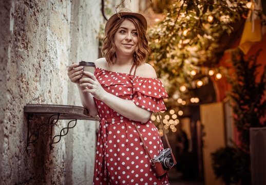 Young stylish woman in vintage clothes with a retro camera drinking coffee on an old european street