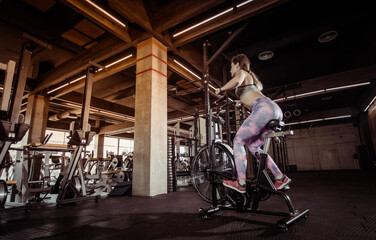 Fototapeta na wymiar Intensive workout fit woman with air bike in gym