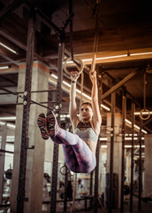 Young athletic woman exercising on gymnastic rings in dark gym
