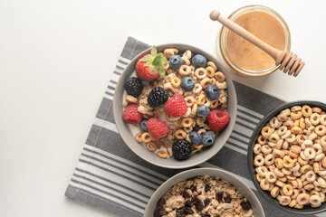Cereal bowls with berries and honey on a gray striped napkin on a white table. Healthy eating concept. Top view.