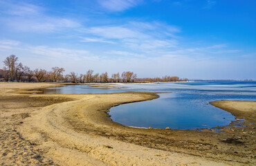 Scenic view of winding shoreline of Dnieper river, Cherkasy, Ukraine at early spring day. Bare trees on background
