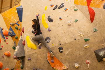 Girl climbing on practical wall indoor, bouldering training