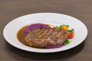 Beef Steak with brown sauce and gilled vegetables on a white plate in wooden table 