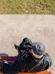 calm older gentleman sitting on a bench in the street. Old age in aerial view
