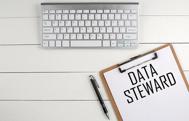 Home office workspace with keyboard, clipboard and pen with text DATA STEWARD on white wooden background , business concept