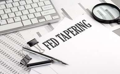 FED TAPERING text on paper with chart and keyboard, business concept