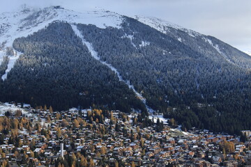 View over the ski resort town of Verbier, Valais, Switzerland in autumn including freshly covered conifer forest on the Swiss alps. Swiss travel landscape screensaver background