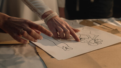 Close-up shot of tailors and woman discussing sketches of wedding dress. Bride on fitting wedding dress in luxury designer atelier or tailoring studio. Concept of fashion, handmade and couturier.