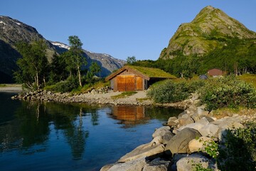 Fototapeta na wymiar Wooden house by lake. Beautiful surroundings of a mountain hut on Lake Gjende in Norway, below the world-famous Besseggen mountain ridge.