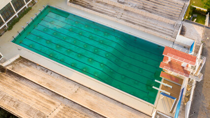 Aerial view of a large swimming pool with lanes and diving boards for diving competitions. The stands are in marble. The sports complex is empty and not playing sports.