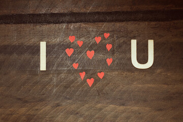 Simple loving dedication on a wooden table made with letters and small red hearts. I love you.