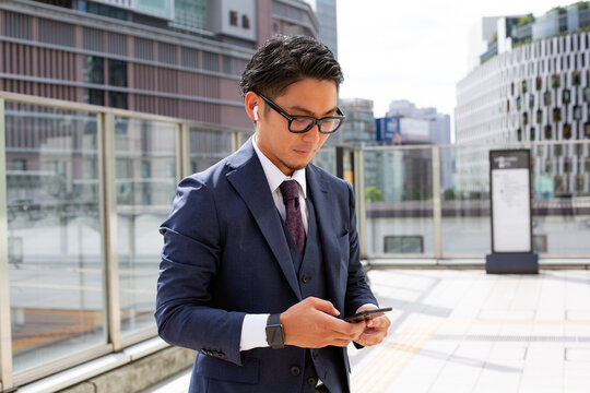 A young businessman in the city, on the move, a man outdoors in a suit looking at his mobile phone.