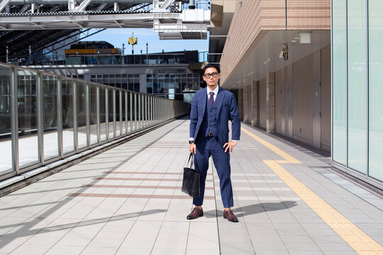 A Young Businessman In The City, On The Move, A Man In A Suit With A Laptop Bag, Standing Legs Apart On A Walkway.