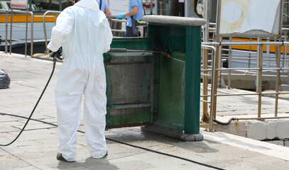 worker with white protective suit during the washing of street furniture with the powerful jet of the pressure washer
