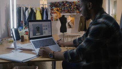 African American fashion designer develops clothes design in 3D modeling program on laptop using...