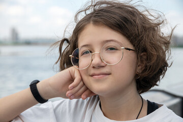 portrait of smiling teenage girl in trendy glasses with curly hair in city park on sunny summer day, cool lifestyle of younger generation, close-up