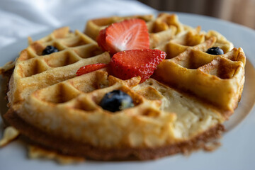 Close up view of a freshly made waffle topped with strawberries and blueberries 