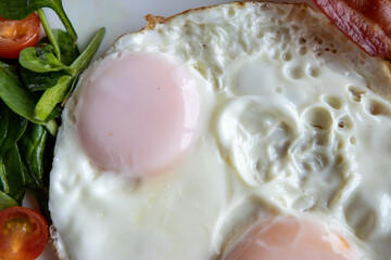 Close up detailed view of over easy eggs and bacon and a white plate