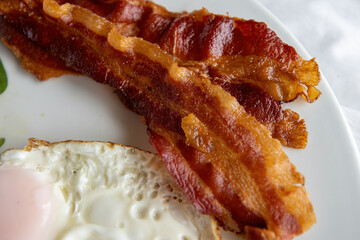 Close up detailed view of over easy eggs and bacon and a white plate