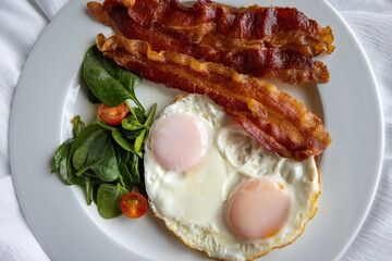 Close up detailed view of over easy eggs and bacon and a white plate