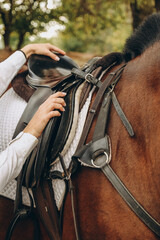 A young woman jockey adjusts the harness on her horse before training.